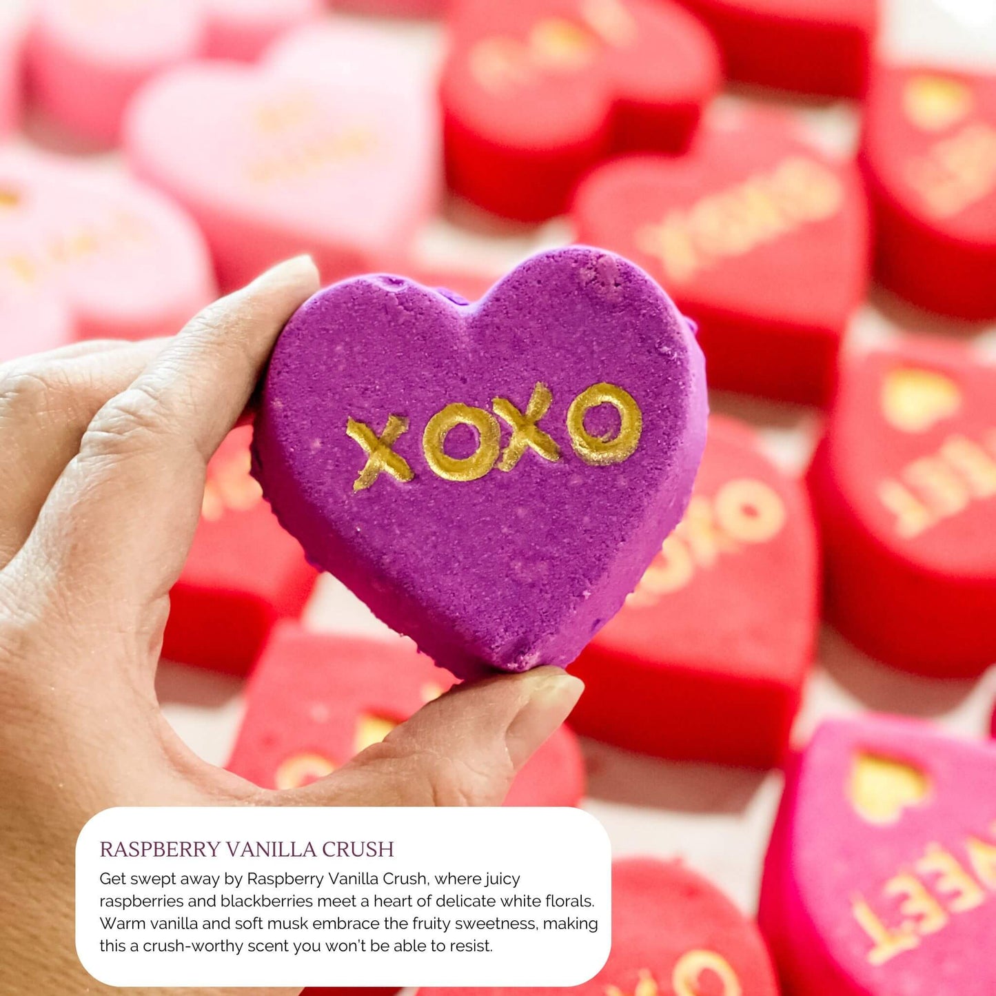 Purple heart-shaped bath bomb with 'XOXO' written in gold, part of the Raspberry Vanilla Crush fragrance from Sweet Temptations Collection.