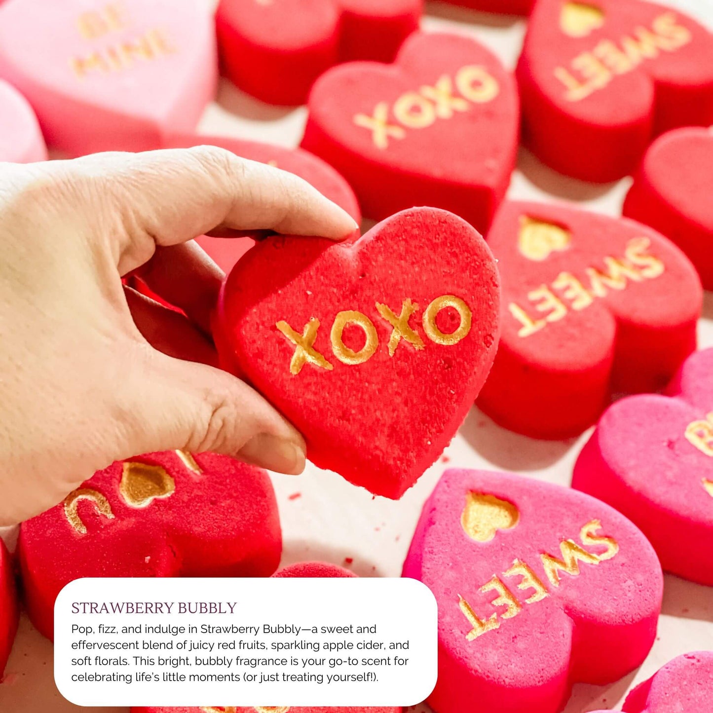 Red heart-shaped bath bomb with 'XOXO' in gold, featuring the effervescent Strawberry Bubbly fragrance from Sweet Temptations Collection.