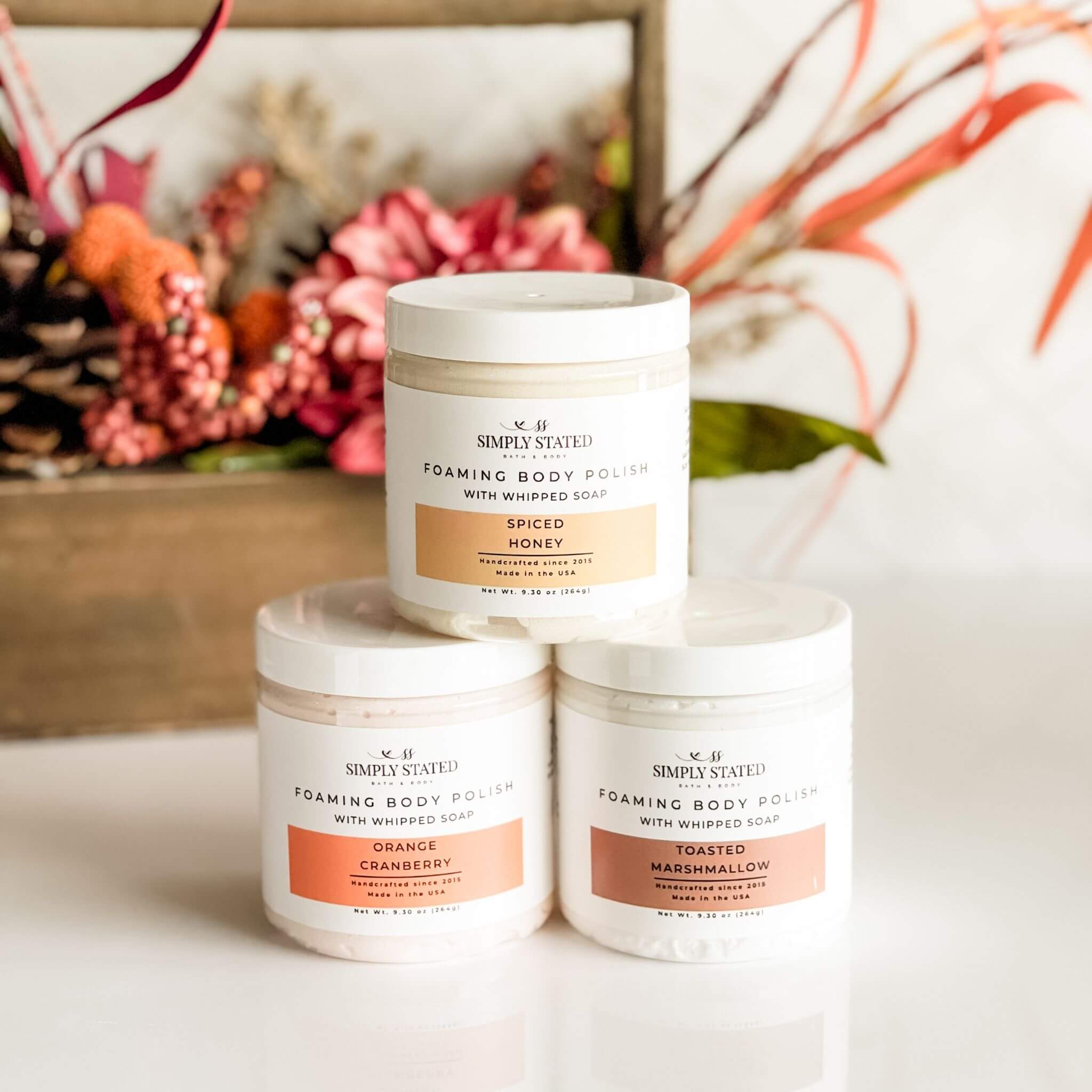 Simply Stated Fall Foaming Body Polish in Orange Cranberry, Spiced Honey, and Toasted Marshmallow with autumn decor