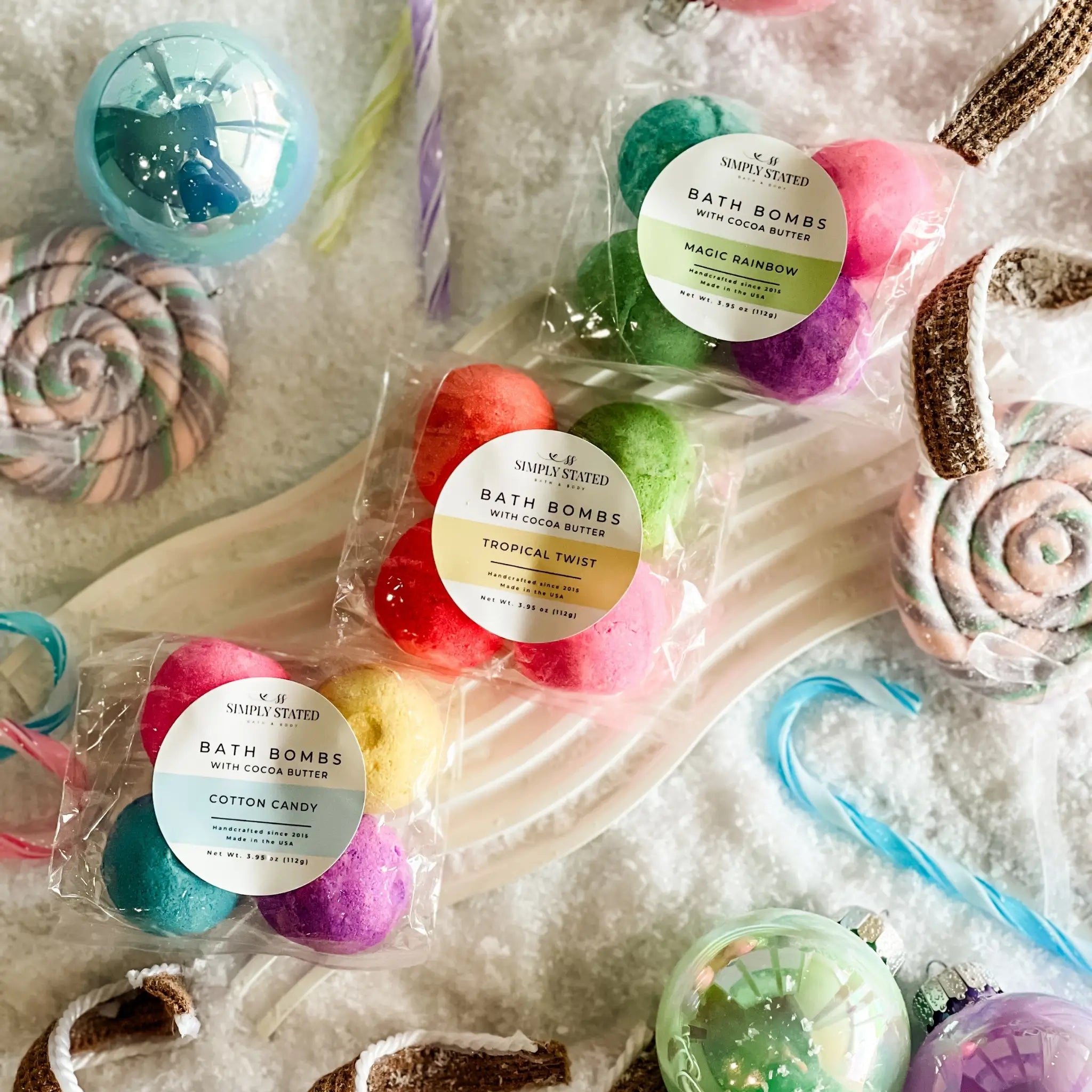 Colorful bath bombs with labels on a textured surface with candy-themed decorations.
