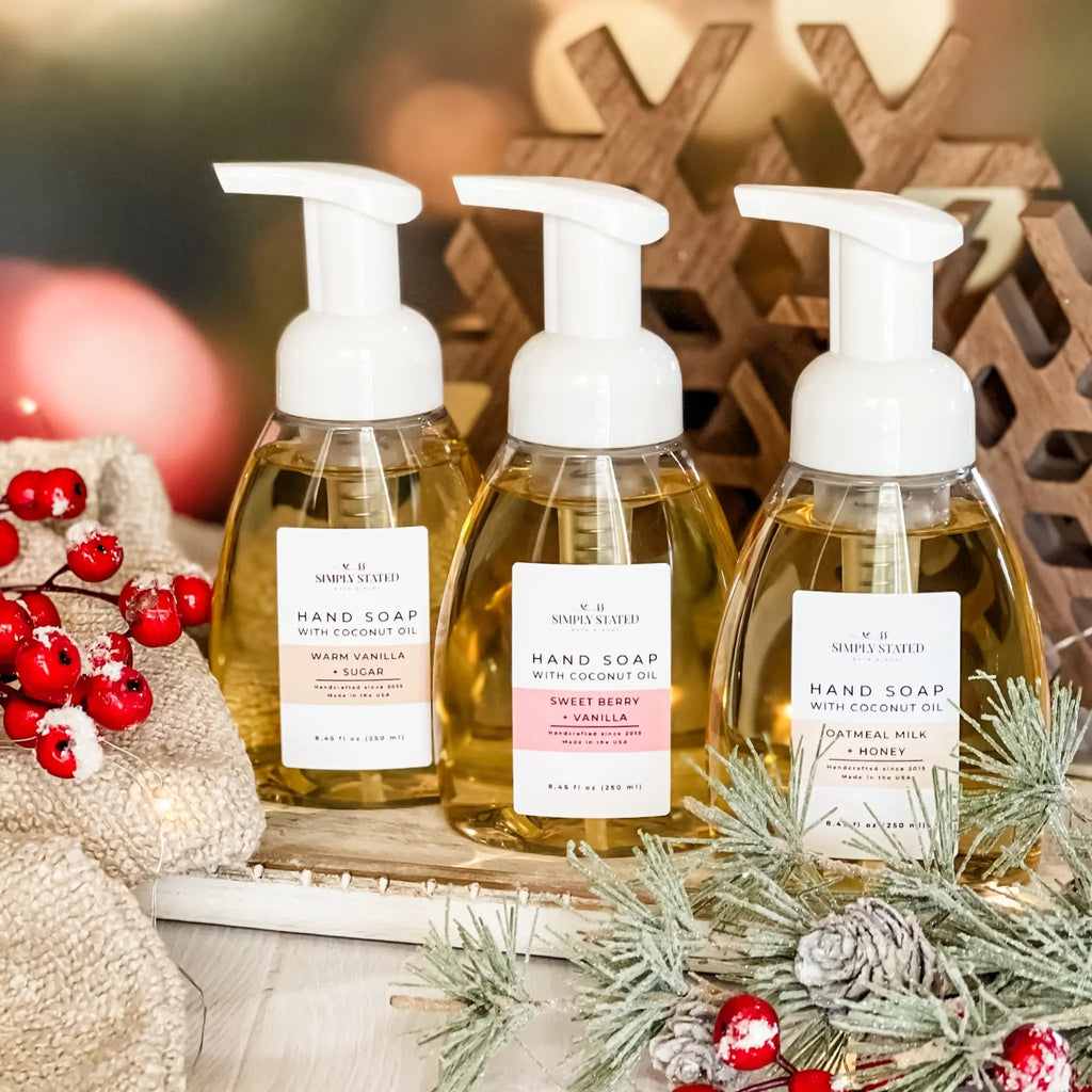 Three bottles of hand soap with pump dispensers on a decorative surface with Christmas elements.