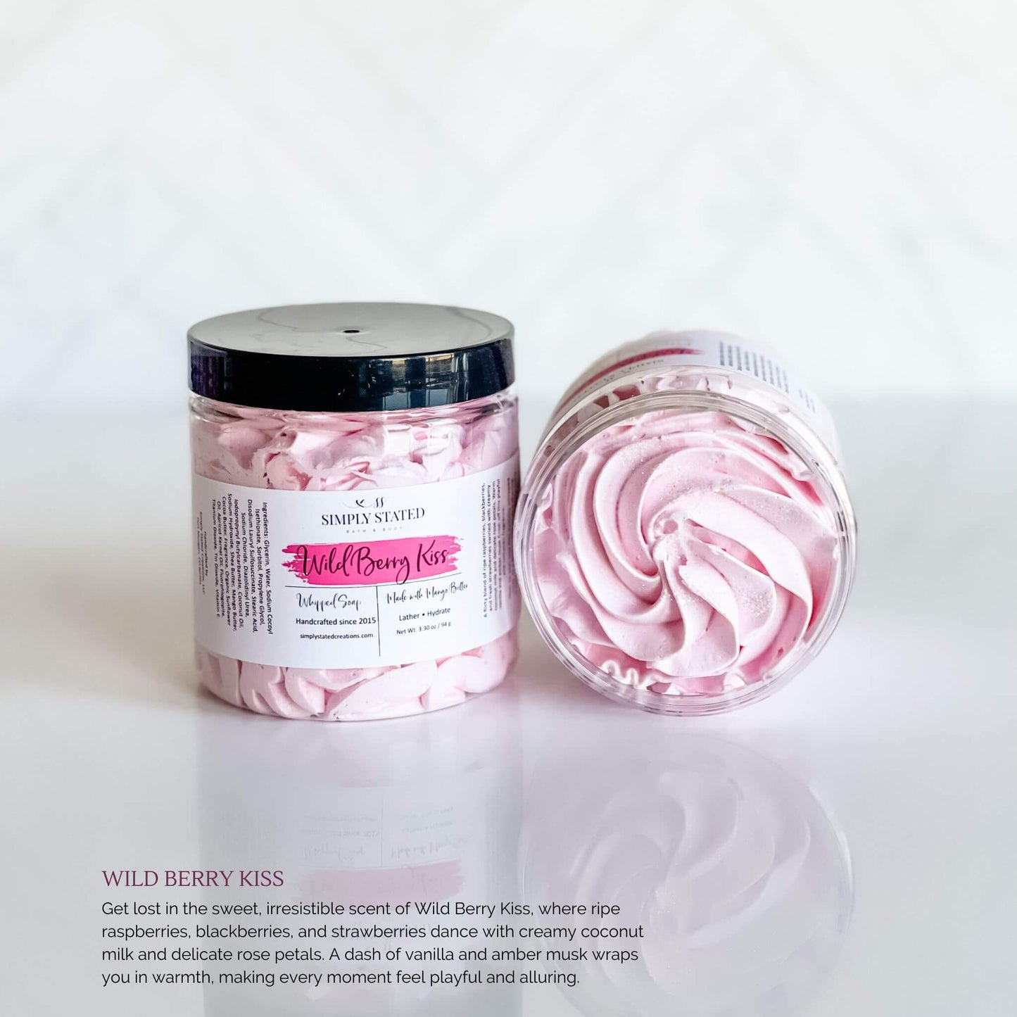 Simply Stated Bath & Body Wild Berry Kiss Whipped Soap in a clear jar with soft pink swirled soap, featuring a magenta label and black lid, displayed on a clean white surface.