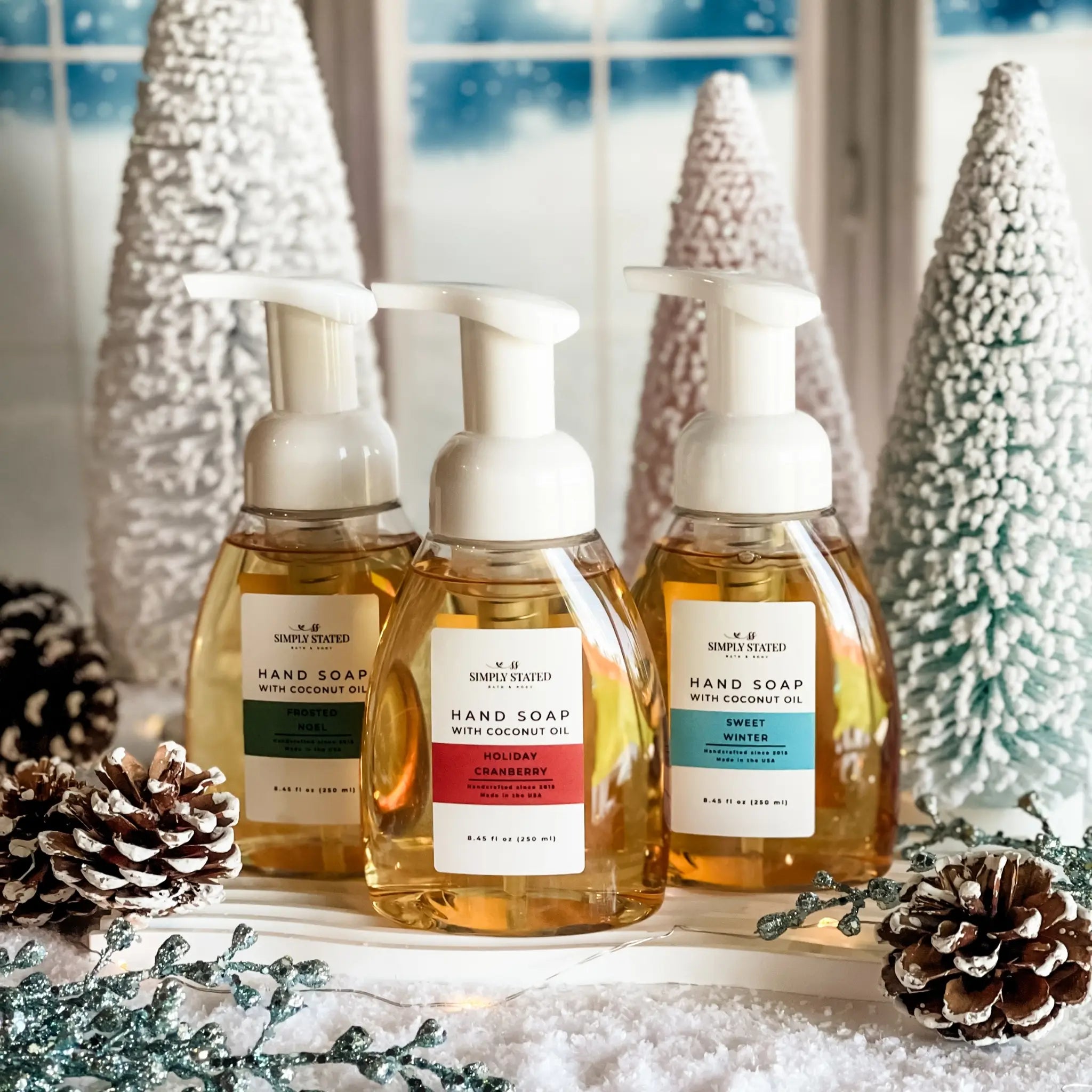 Three bottles of hand soap with decorative Christmas trees and pinecones in the background.