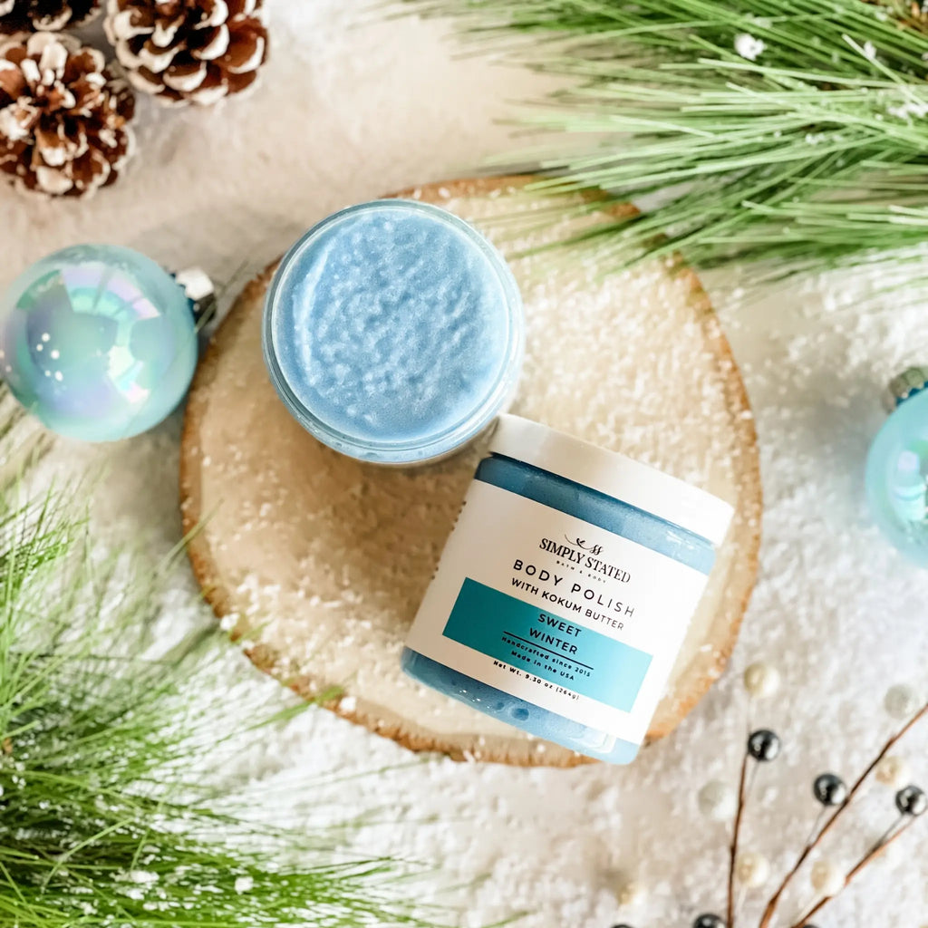 Two jars of body polish on a decorative surface with greenery and ornaments.